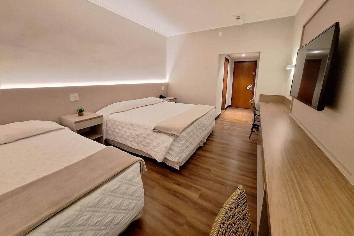 A modern hotel room with two beds, a flat-screen TV, and a wooden floor.