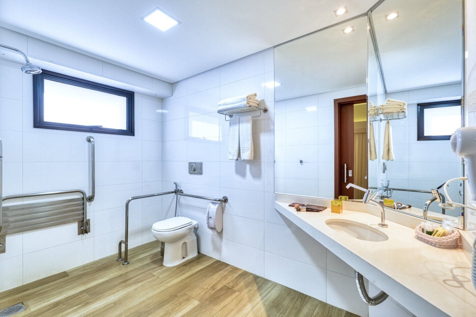 Une salle de bain moderne équipée de toilettes, de barres d’appui, d’un lavabo et d’un grand miroir.