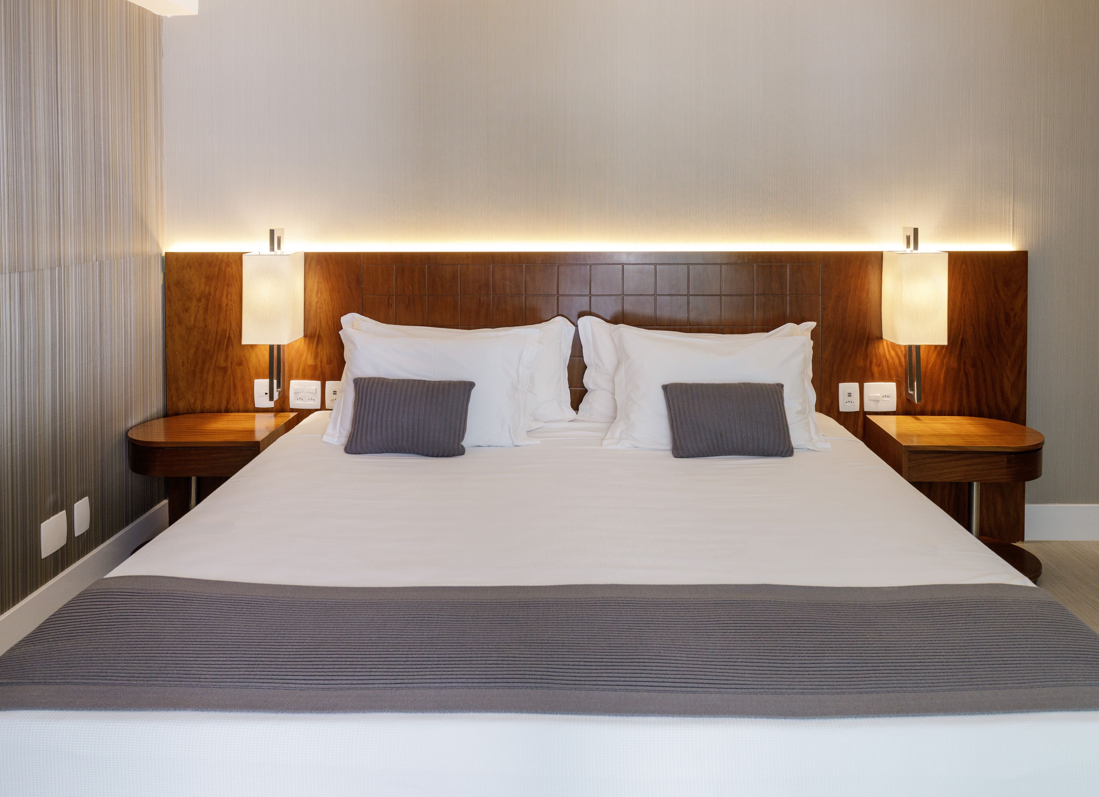A hotel room with a large bed, two bedside tables, and two wall-mounted lamps.