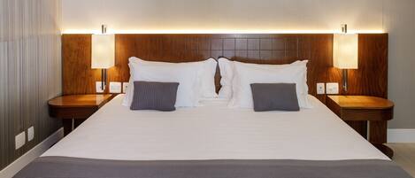 A hotel room with a large bed, two bedside tables, and two wall-mounted lamps.