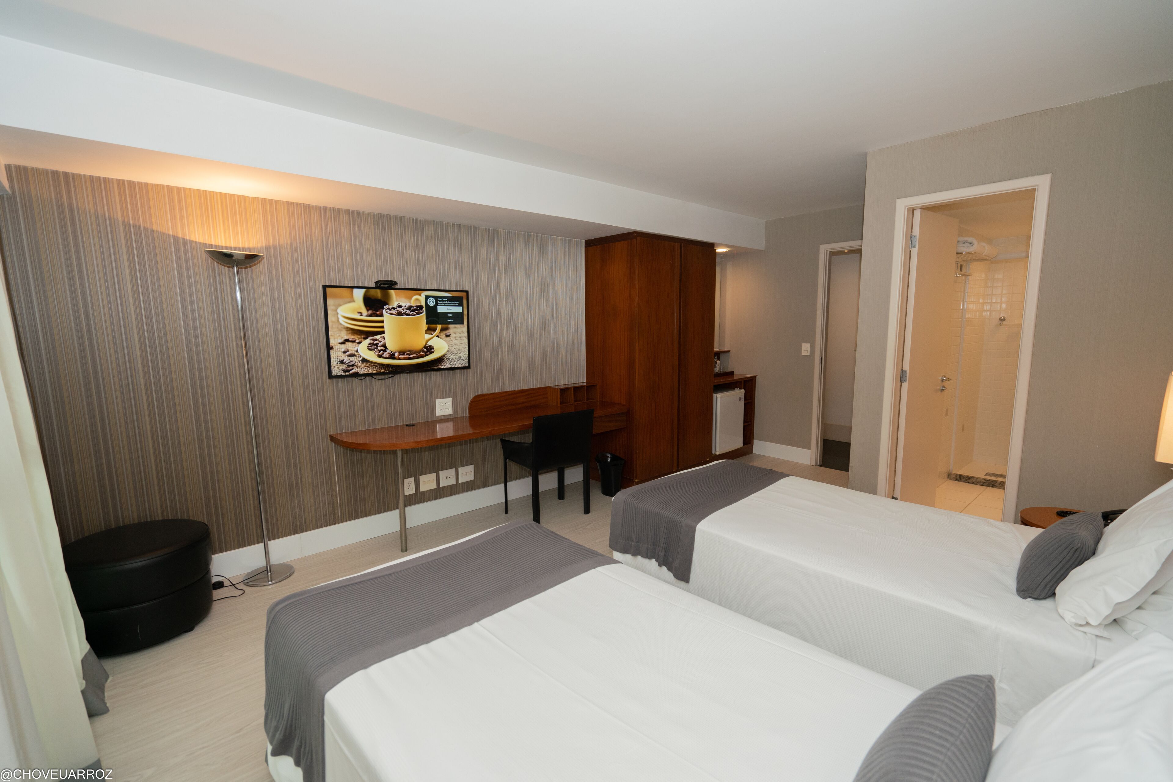 Habitación de hotel con dos camas, un escritorio, una silla, un televisor y una puerta que da a un baño.