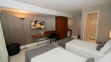Habitación de hotel con dos camas, un escritorio, una silla, un televisor y una puerta que da a un baño.