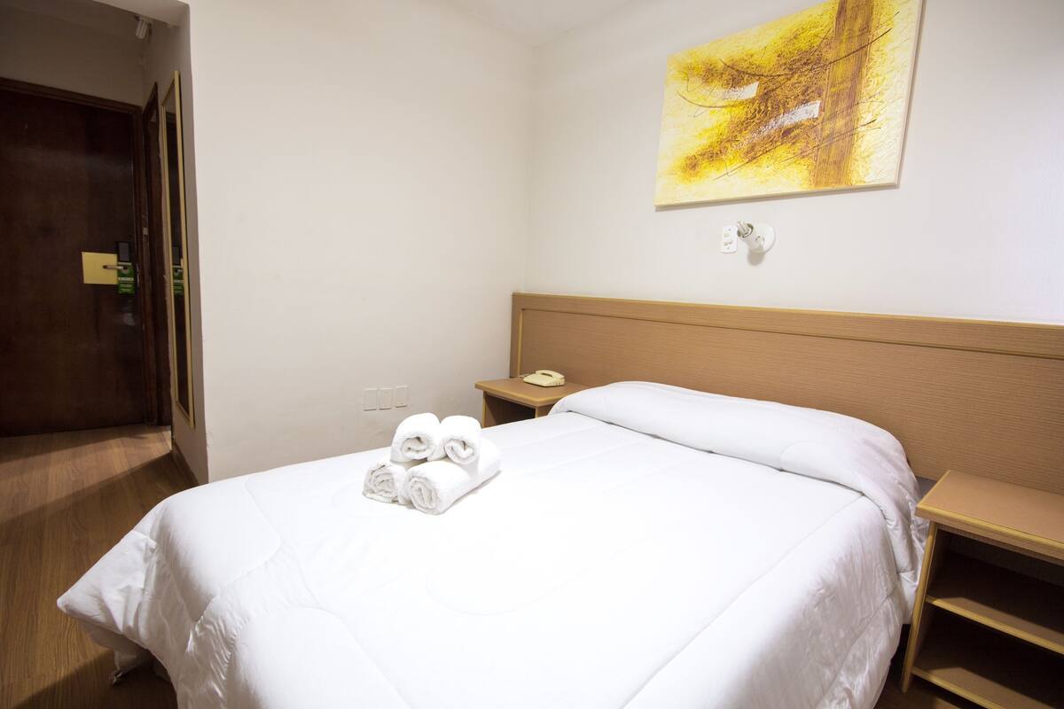 A hotel room with a neatly made bed, a bedside table with a lamp, and a painting on the wall.
