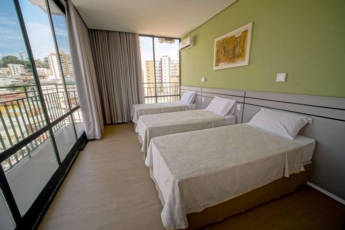 A hotel room with two beds, a large window with a view of the city, and a painting on the wall.