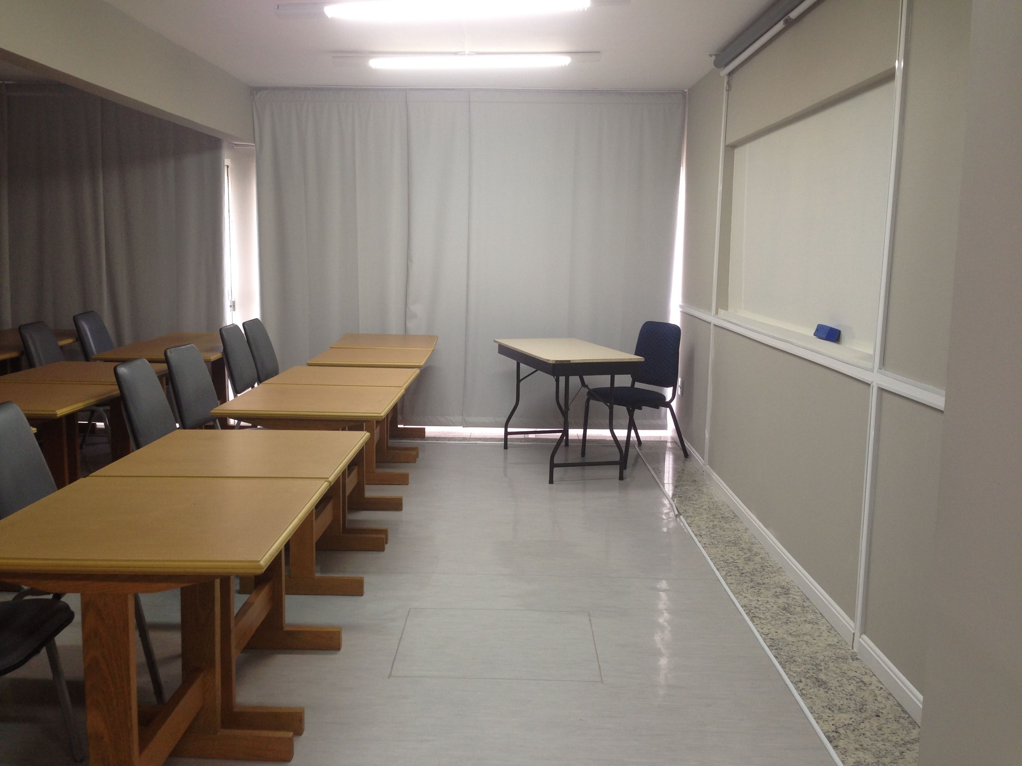 A conference room with long tables and chairs, a projector screen, and a large window with curtains.