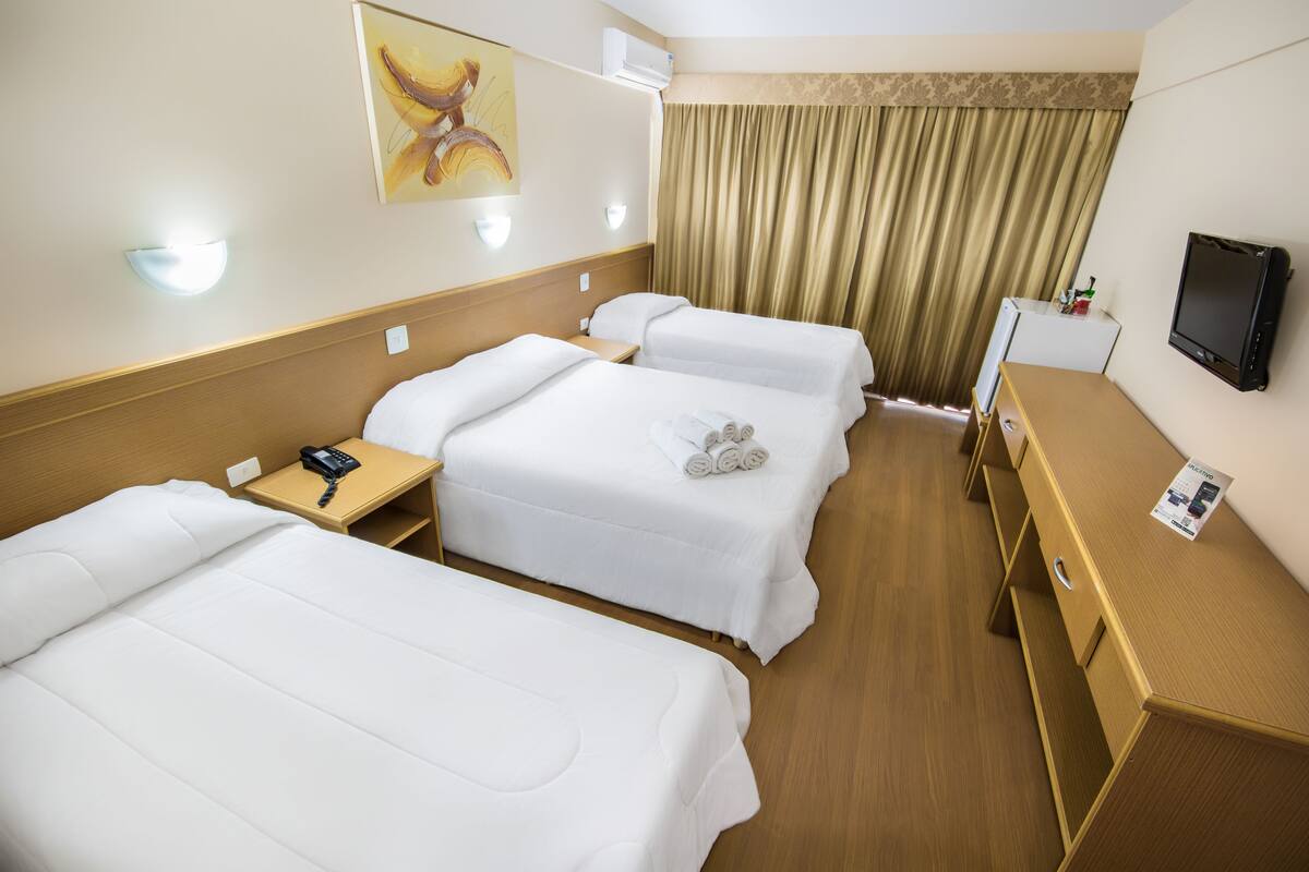 A hotel room with two beds, a desk, a TV, and a painting on the wall.