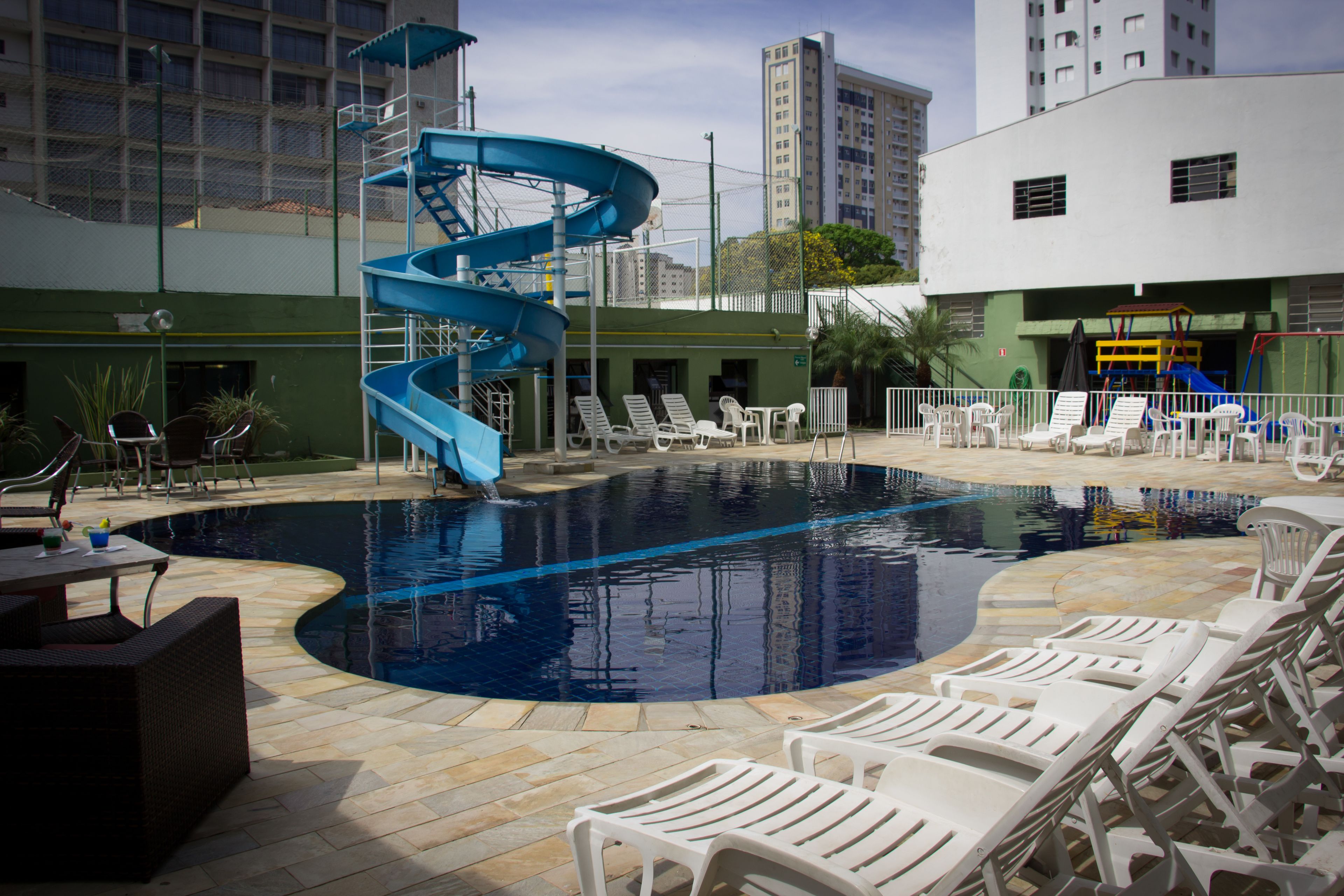 A swimming pool with a blue spiral slide, surrounded by white lounge chairs and a small table.