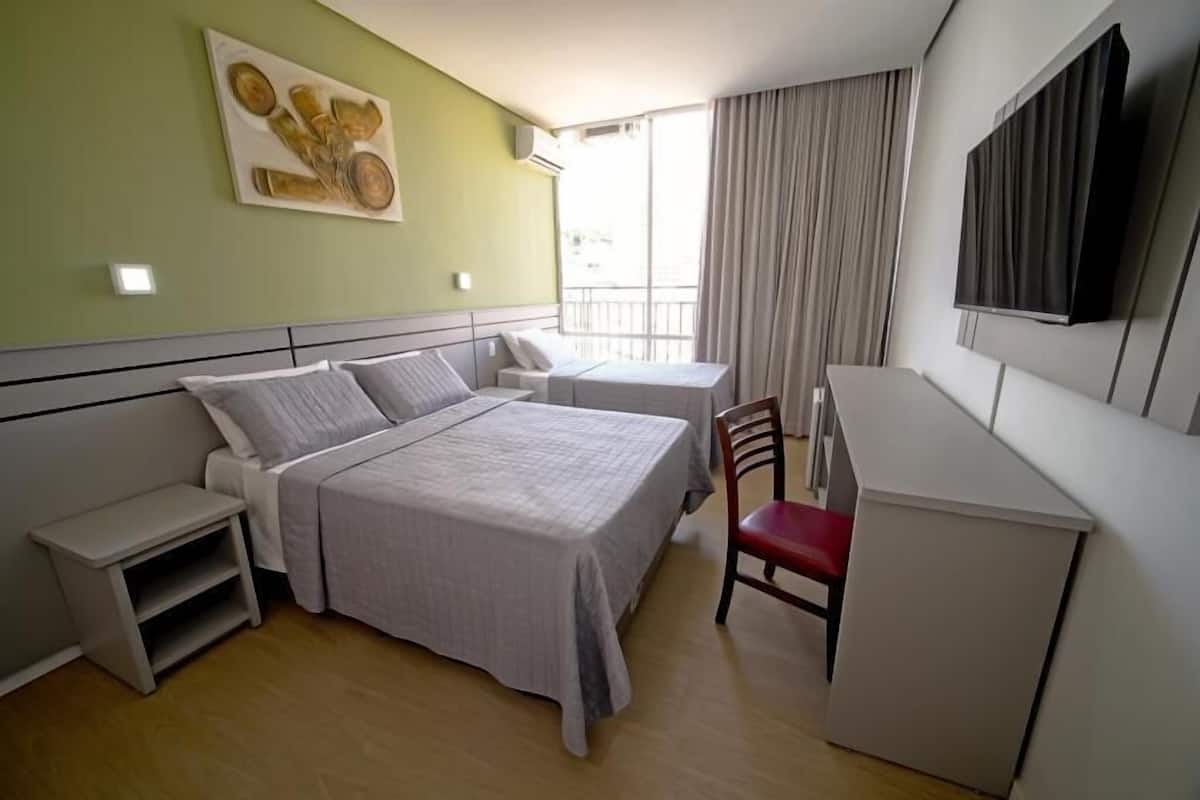 A hotel room with a bed, a desk, a chair, a TV, and a painting on the wall.