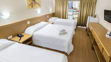 A hotel room with two beds, a desk, a TV, and a window with curtains.
