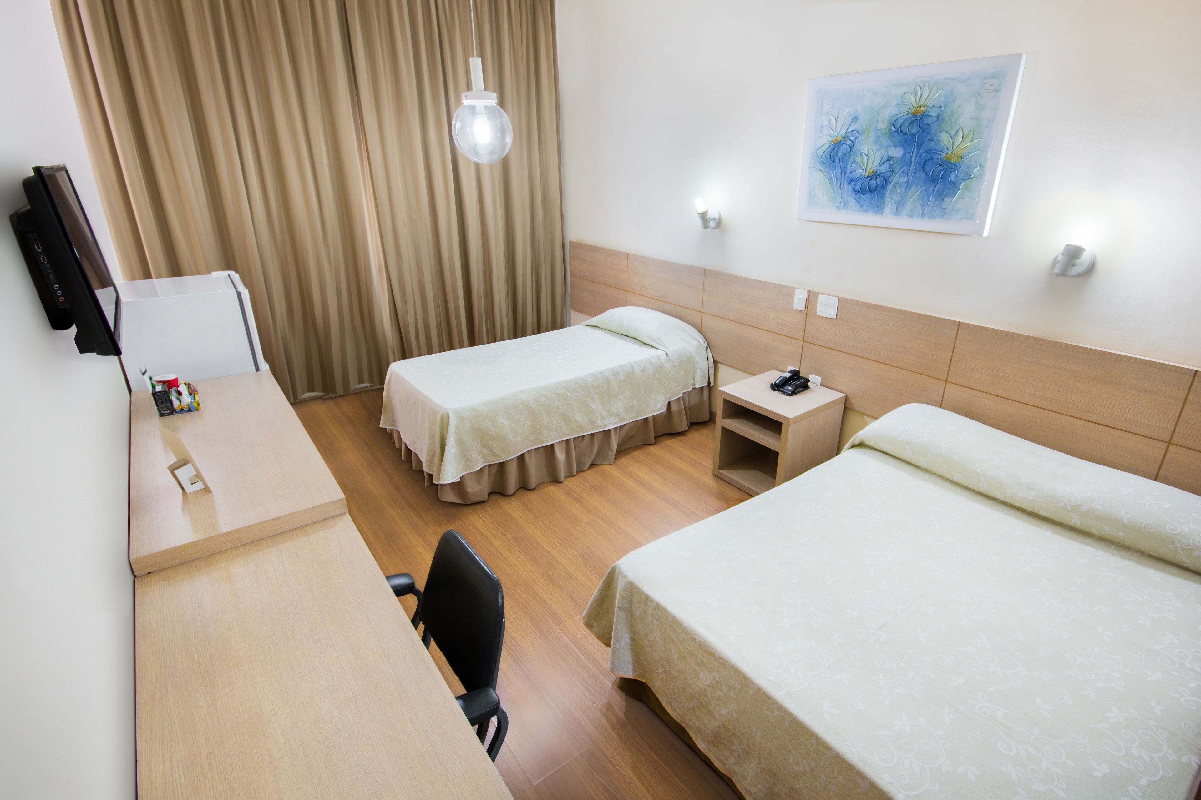 Ett hotellrum med två separata sängar, ett skrivbord med en stol, en tv och en tavla på väggen.