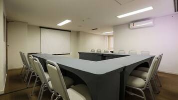 Uma sala de conferências com uma mesa comprida, seis cadeiras e uma tela de projetor.