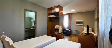 A hotel room with two beds, a desk, a chair, a wardrobe, and a bathroom.