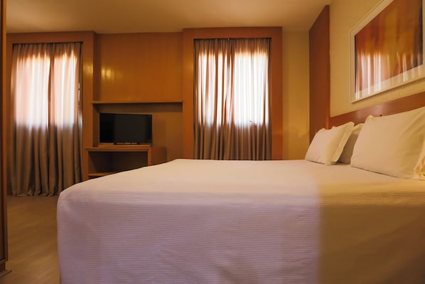 Una habitación de hotel con una cama grande, un televisor de pantalla plana y cortinas.