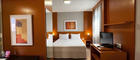 A hotel room with a bed, a desk with a computer, a TV, and artwork on the walls.
