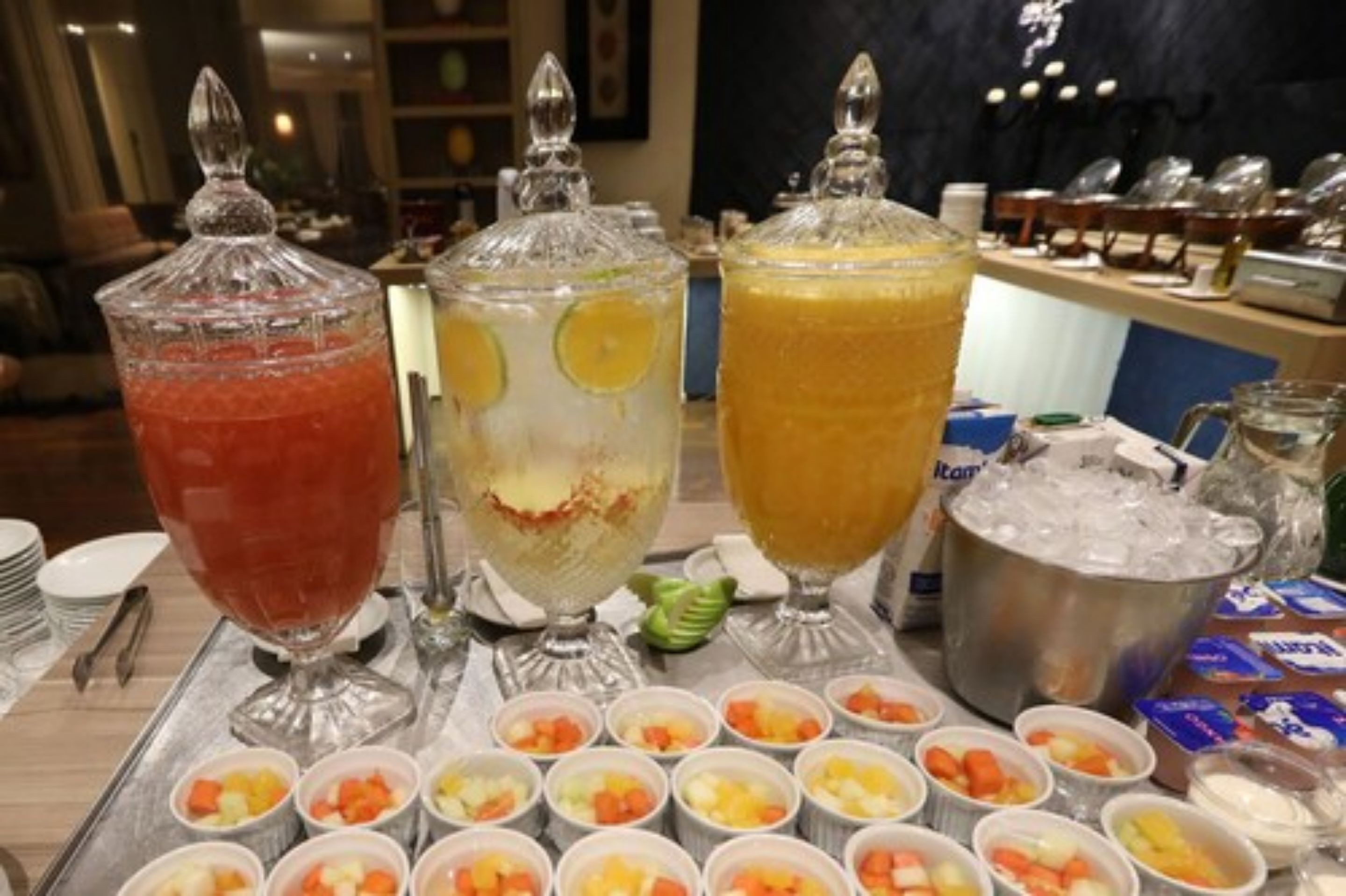 A buffet setup with three large punch bowls and various small bowls of fruit.