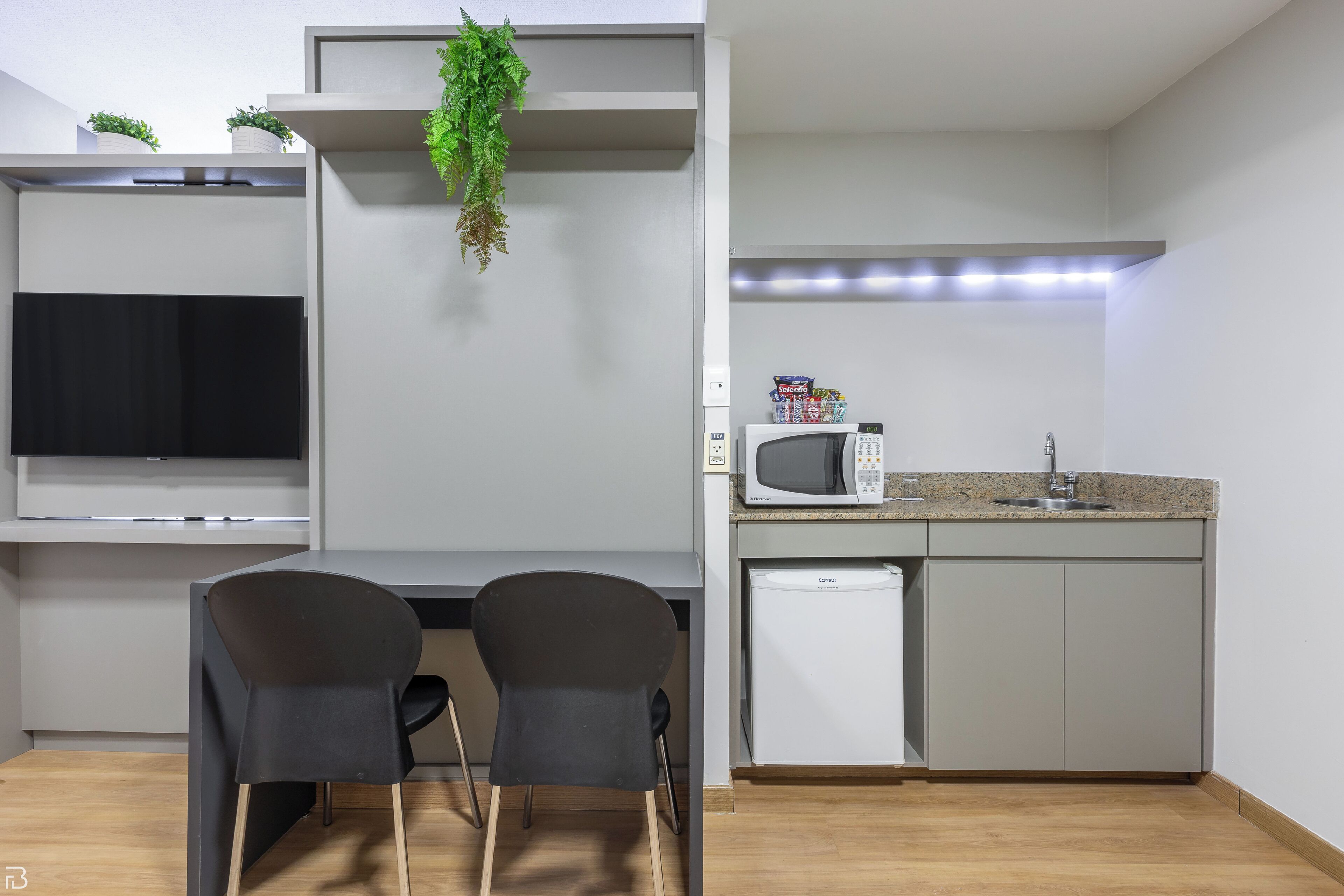 Een moderne keuken met een magnetron, spoelbak en een flatscreen televisie.