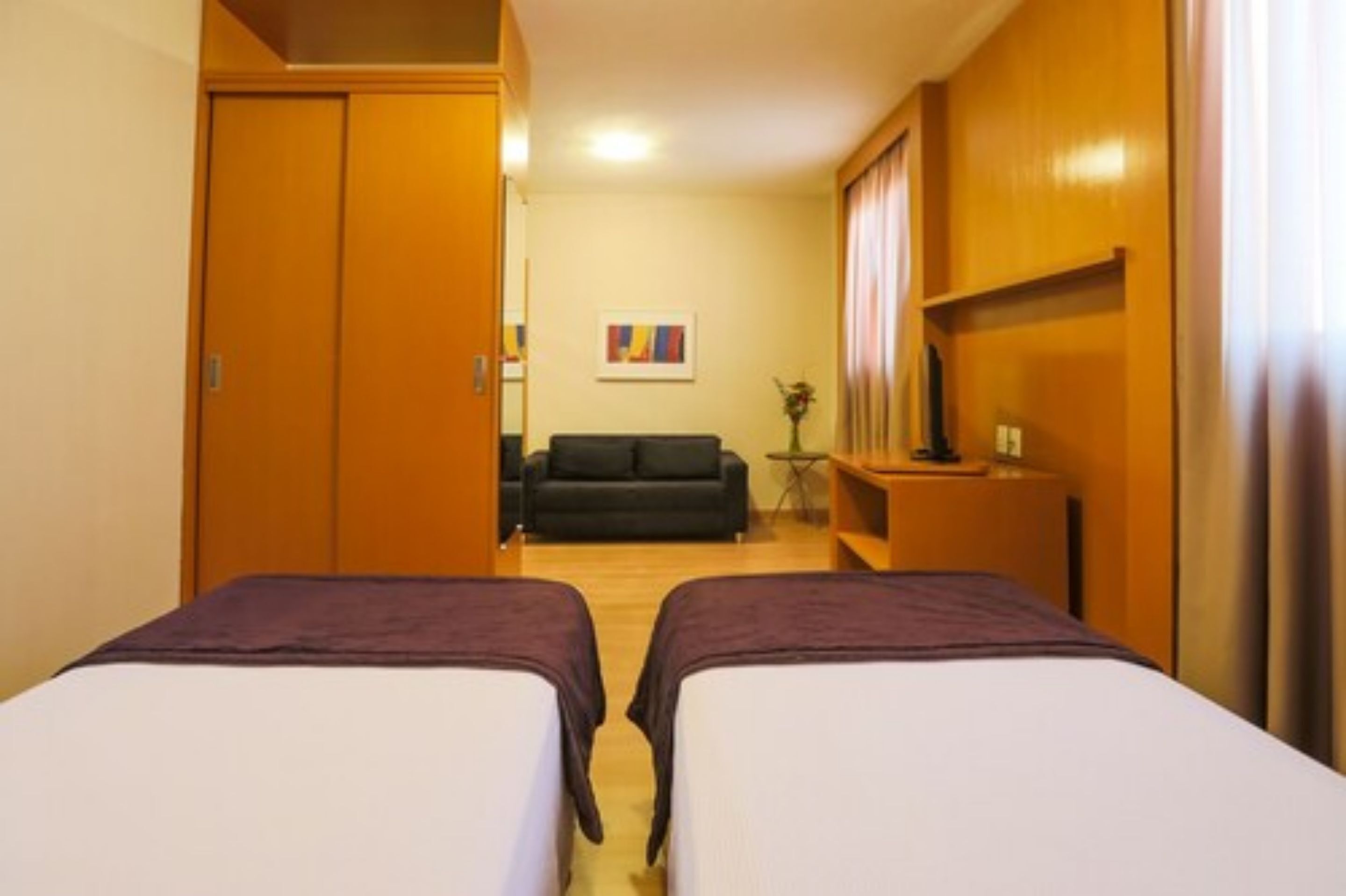 Een hotelkamer met twee bedden, een bank, een televisie en een kleine tafel met een vaas.