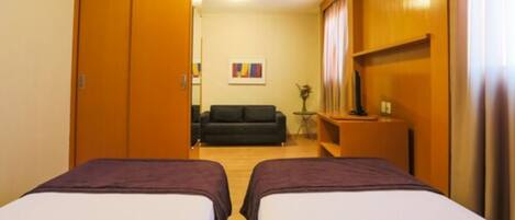 Une chambre d’hôtel avec deux lits, un canapé, une télévision et une petite table sur laquelle se trouve un vase.