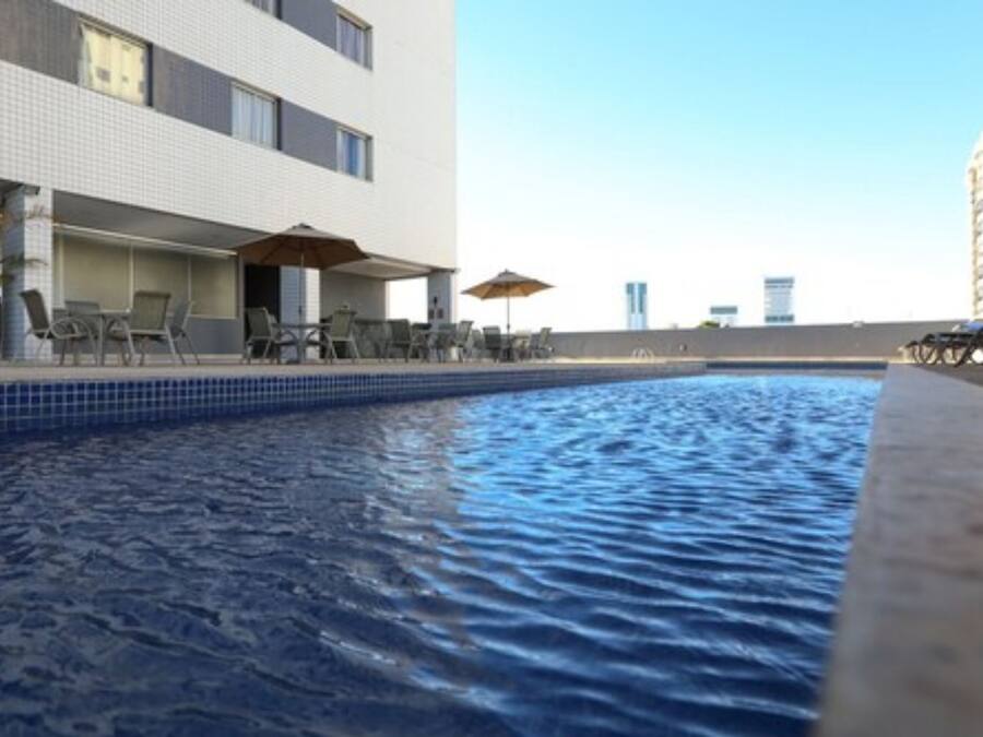 A rooftop pool with lounge chairs and umbrellas, surrounded by a modern building with a tiled exterior.