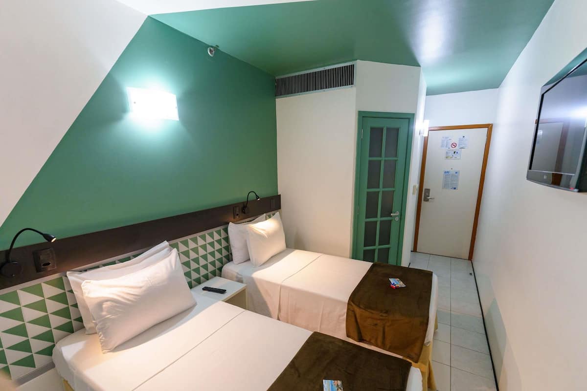 A hotel room with two beds, a small table, a TV, and a door with a green frame.