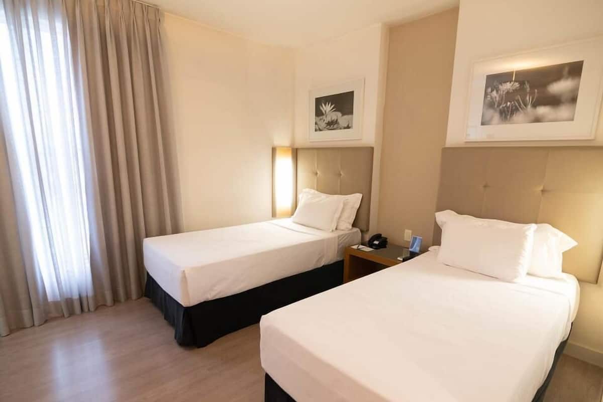 A hotel room with two beds, a nightstand, and two framed pictures on the wall.