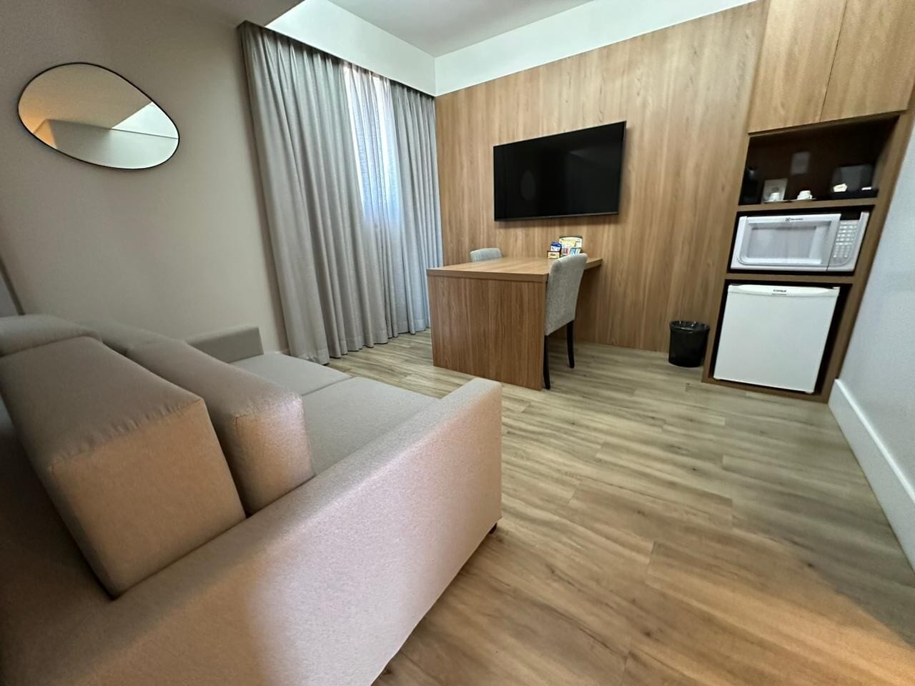 A modern living room with a sofa, a flat-screen TV, a wooden desk, and a microwave.