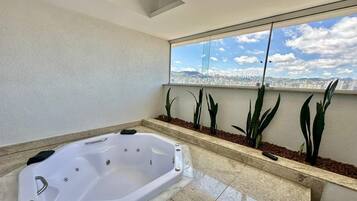 A modern bathroom with a large bathtub, a window with a city view, and decorative plants.