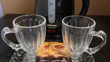 Dos vasos de vidrio transparente sobre una superficie texturizada, una tetera eléctrica negra y dos sobres de crema.