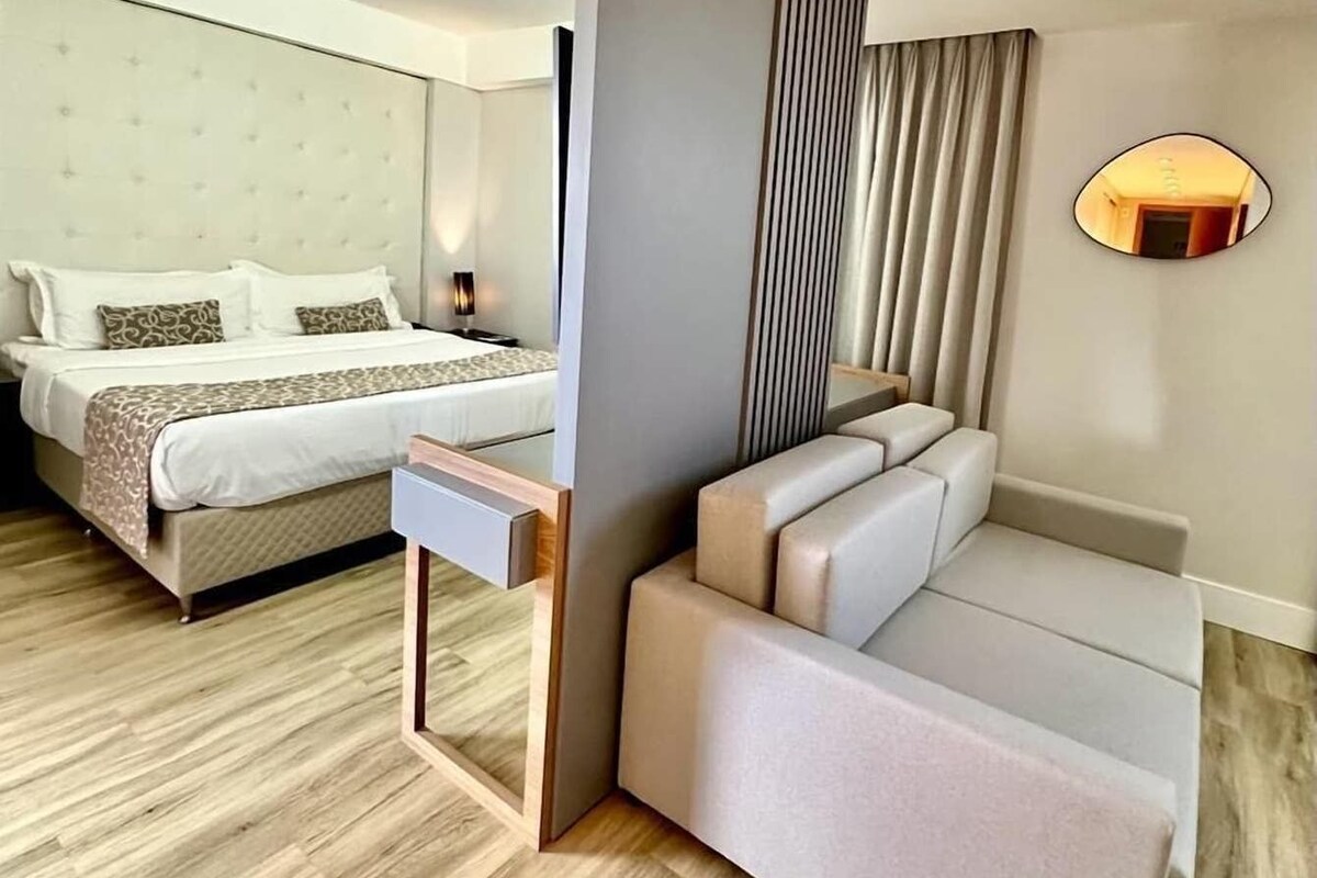 Una habitación de hotel moderna con una cama, un sofá, una mesita y un espejo montado en la pared.