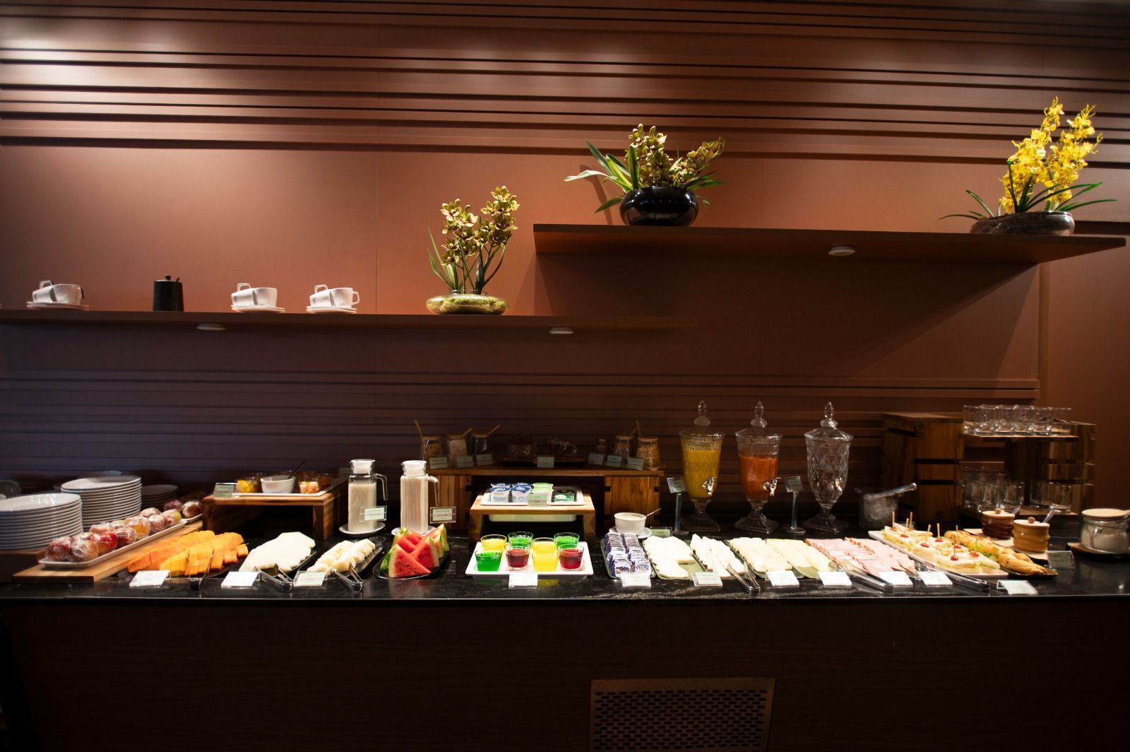 Buffet com diversos alimentos e bebidas, incluindo frutas, sanduíches e uma seleção de sucos.