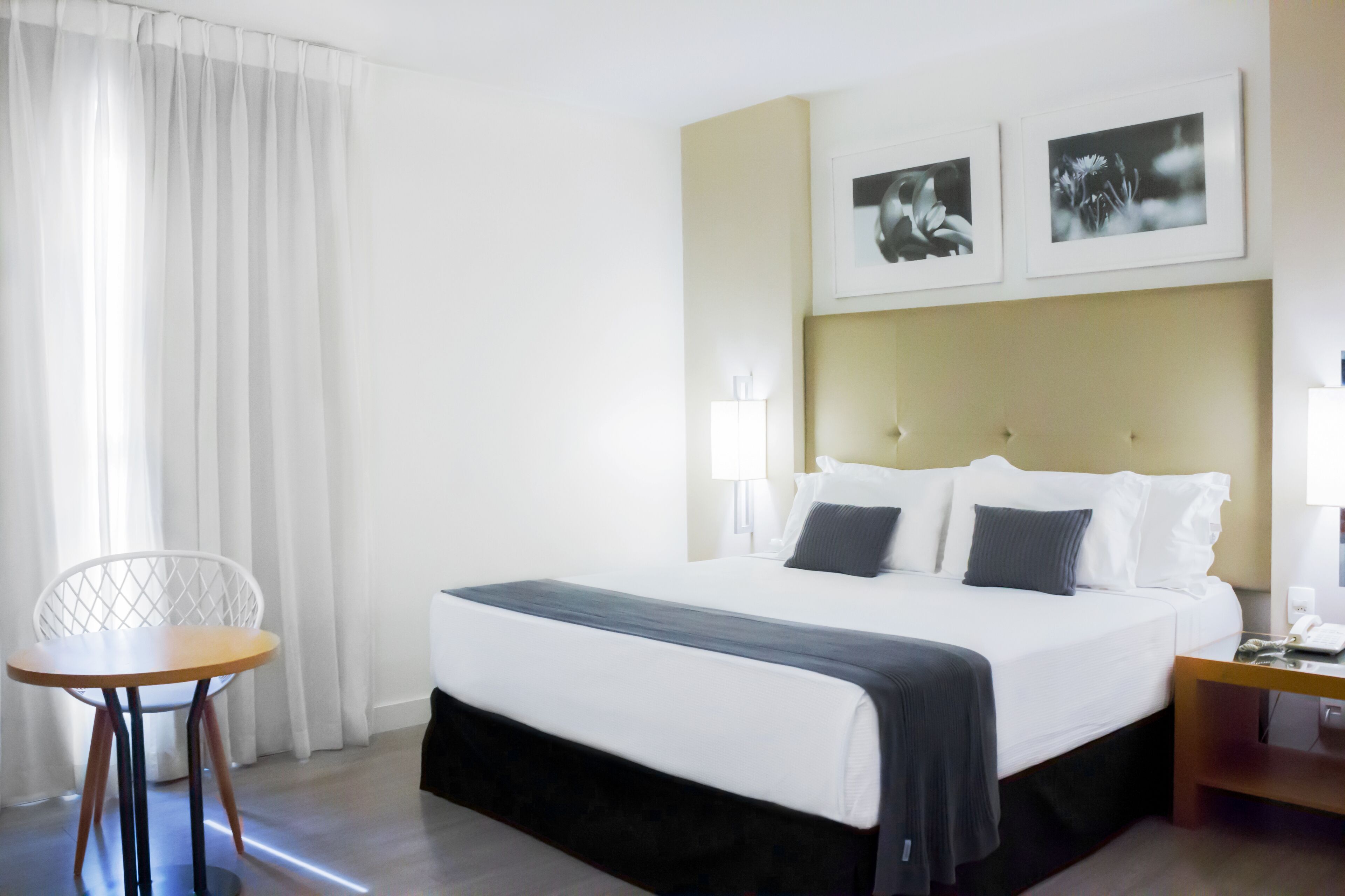 A hotel room with a bed, a chair, a bedside table, and two framed pictures on the wall.