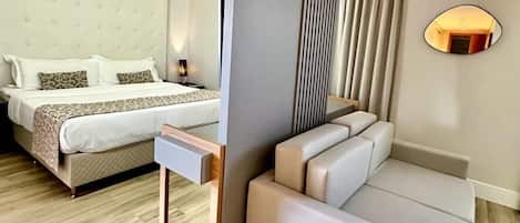 A modern hotel room with a large bed, a sofa, a small table, and a mirror on the wall.