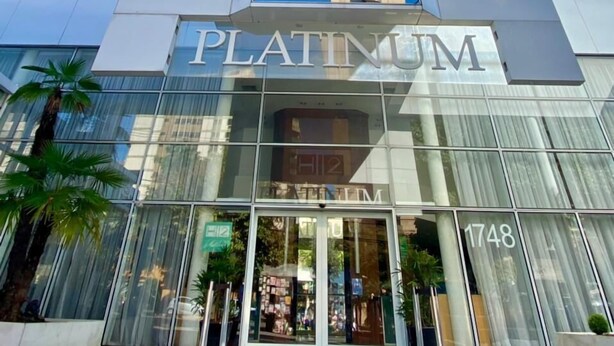 Een modern hotel met een opvallend 'Platinum'-bord, grote glasramen en een heldere lucht.
