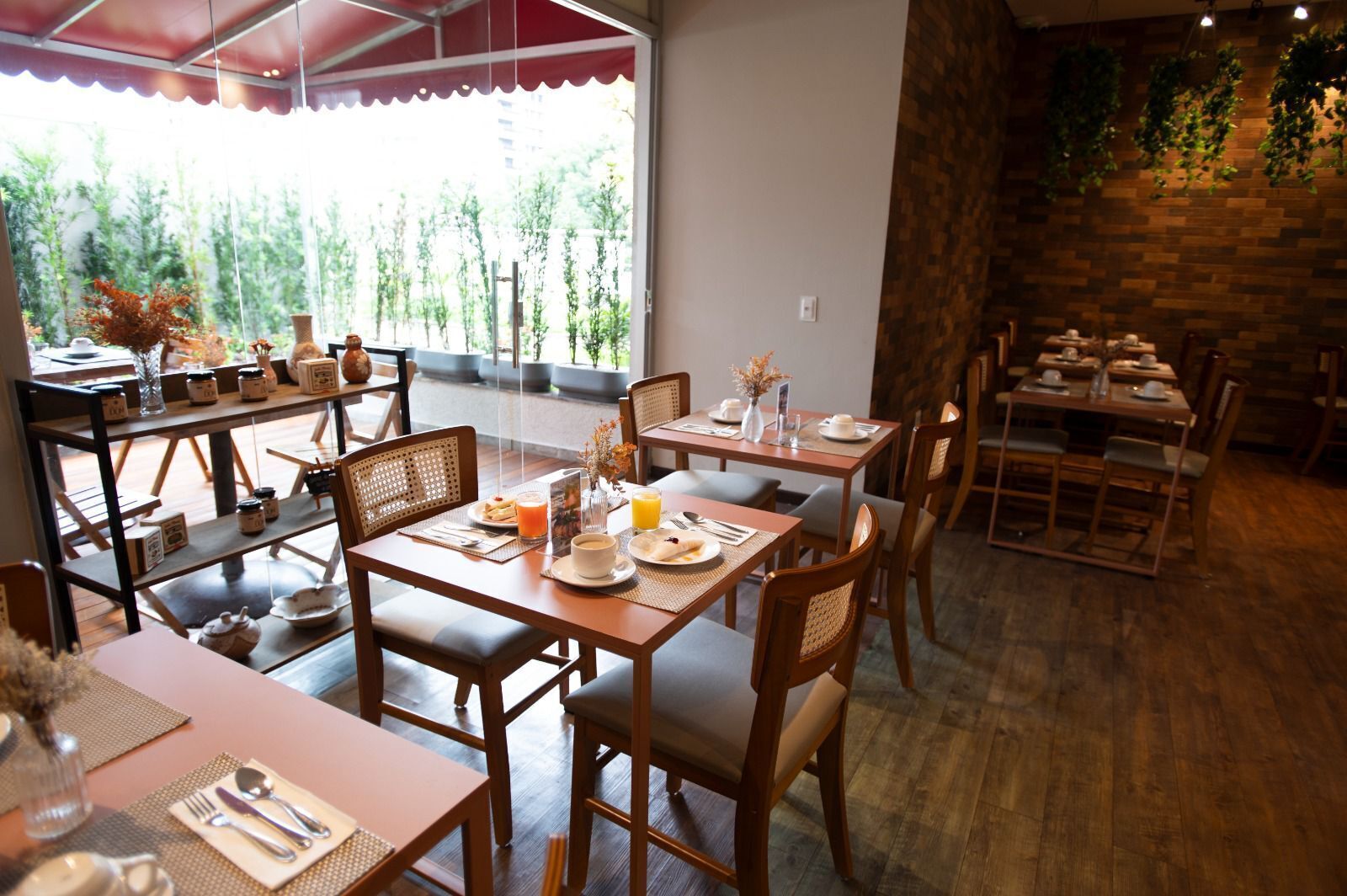 A restaurant with wooden tables and chairs, a stone wall, and a view of greenery outside.