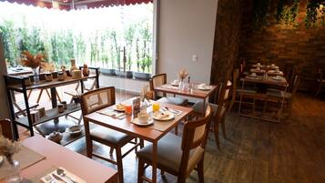 A restaurant with wooden tables and chairs, a stone wall, and a view of greenery outside.