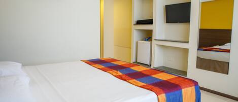 Una habitación de hotel con cama, televisor, armario y una pequeña kitchenette.