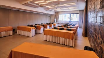 A conference room with rows of tables, chairs, and a large window with curtains.