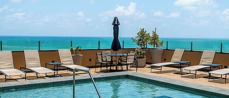A pool area with lounge chairs and a view of the ocean.
