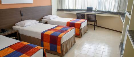 A hotel room with three beds, a desk with a laptop, and a window with curtains.