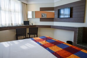 A hotel room with a bed, a desk with a computer, two chairs, a TV mounted on the wall, and a window with curtains. - Park Hotel (Recife)