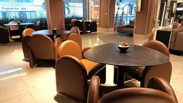 A modern hotel lobby with round tables and leather chairs, a reception desk, and a large window with a view.