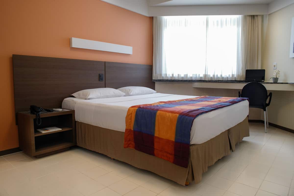 A hotel room with a bed, a desk with a laptop, a chair, and a telephone on a nightstand.