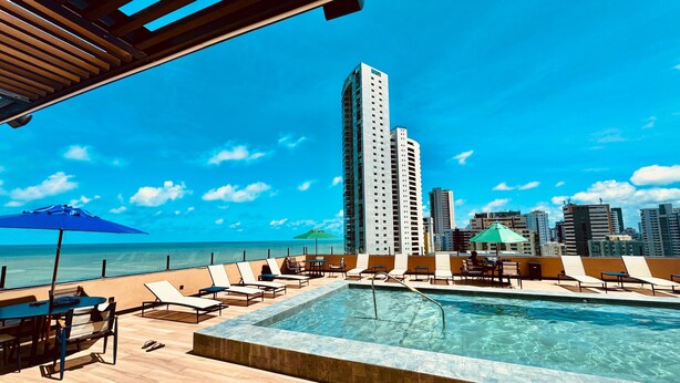 A rooftop pool with lounge chairs and umbrellas, overlooking a city skyline and the ocean. - Park Hotel (Recife)