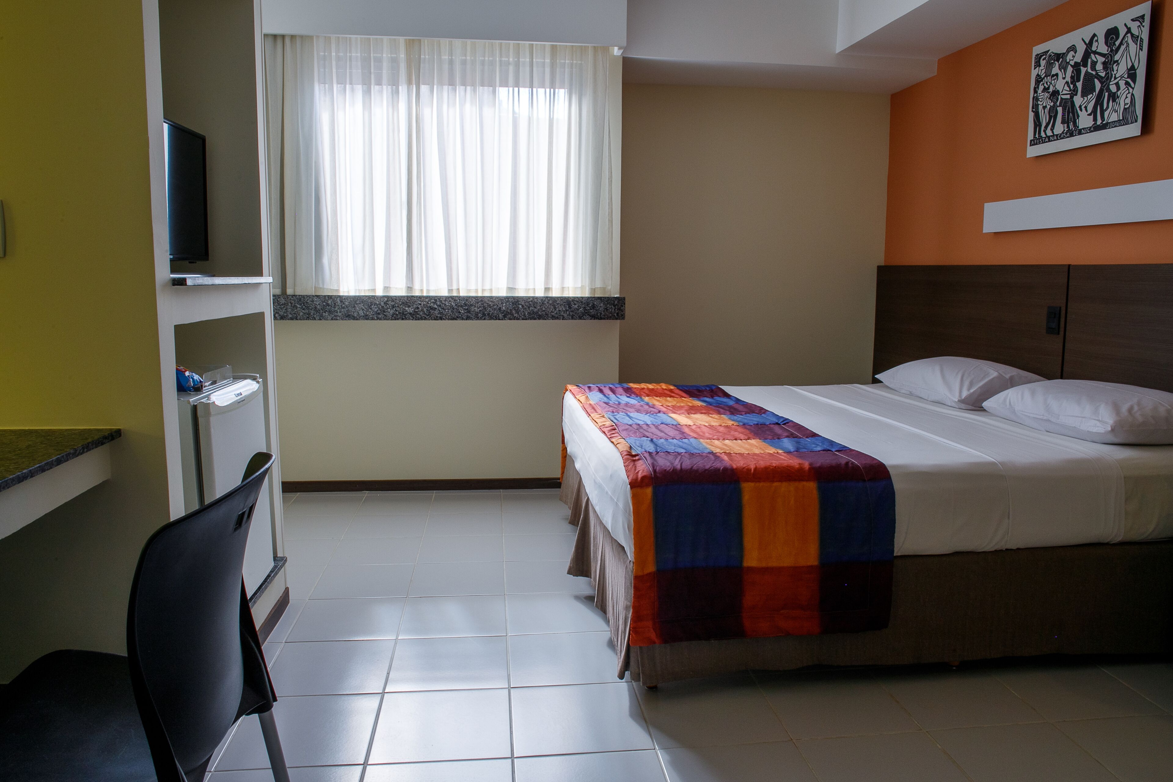 Habitació d'hotel amb llit, escriptori, cadira, televisió i finestra amb cortines.