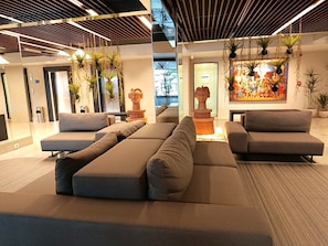 A modern lounge area with a large sectional sofa, a coffee table, and a decorative wall with a painting. - Park Hotel (Recife)
