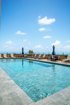 A pool area with lounge chairs and umbrellas, overlooking a clear blue sky and ocean.