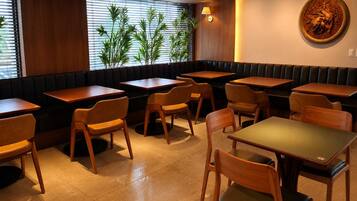 A restaurant interior with booths and tables, wooden chairs, a wall-mounted lamp, and a window with blinds.
