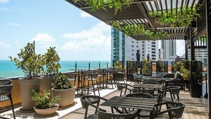An outdoor terrace with tables and chairs, potted plants, and a view of the ocean. - Park Hotel (Recife)