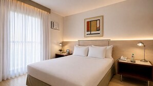 A hotel room with a large bed, two bedside tables, a lamp, a phone, a bottle, and a framed picture on the wall. - Promenade Pancetti Belo Horizonte (Belo Horizonte)