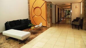 A hotel lobby with a sofa, ottoman, and a coffee table with a vase and papers. - Promenade Pancetti Belo Horizonte (Belo Horizonte)